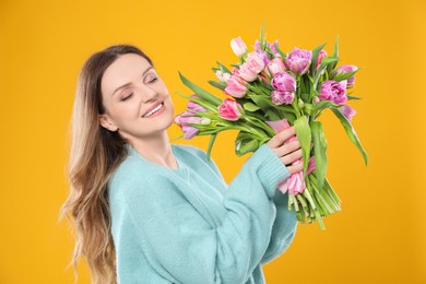 Photo of Happy young woman with bouquet of beautiful tulips on yellow background