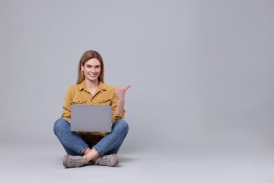 Happy woman with laptop pointing at something on light grey background. Space for text