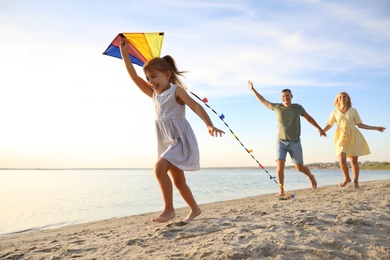 Photo of Happy parents with their child playing with kite on beach. Spending time in nature