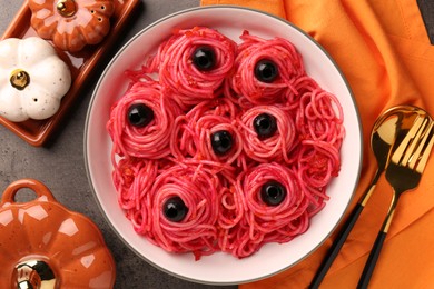 Red pasta with olives in bowl on grey textured table, flat lay. Halloween food