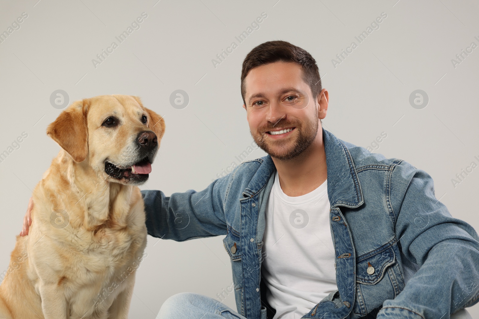 Photo of Man hugging with adorable Labrador Retriever dog on light gray background. Lovely pet