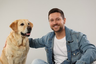 Photo of Man hugging with adorable Labrador Retriever dog on light gray background. Lovely pet