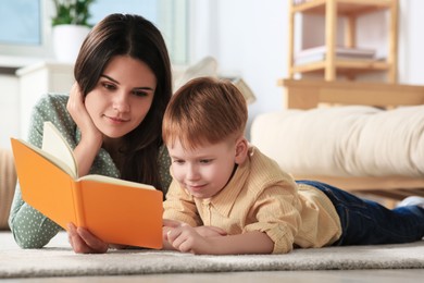 Photo of Mother reading book with her son on floor in living room at home
