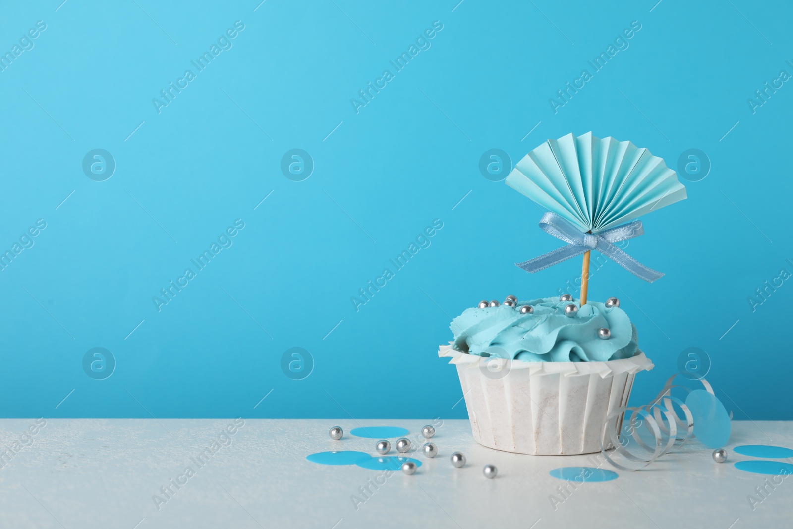Photo of Baby shower cupcake with topper on white table against light blue background, space for text