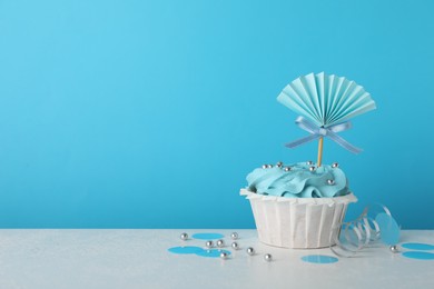 Baby shower cupcake with topper on white table against light blue background, space for text
