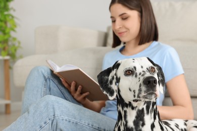 Photo of Beautiful woman reading book and her adorable Dalmatian dog on floor at home, selective focus. Lovely pet