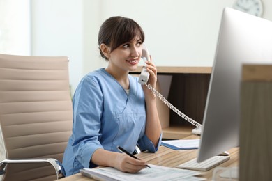 Photo of Smiling medical assistant talking by phone in office