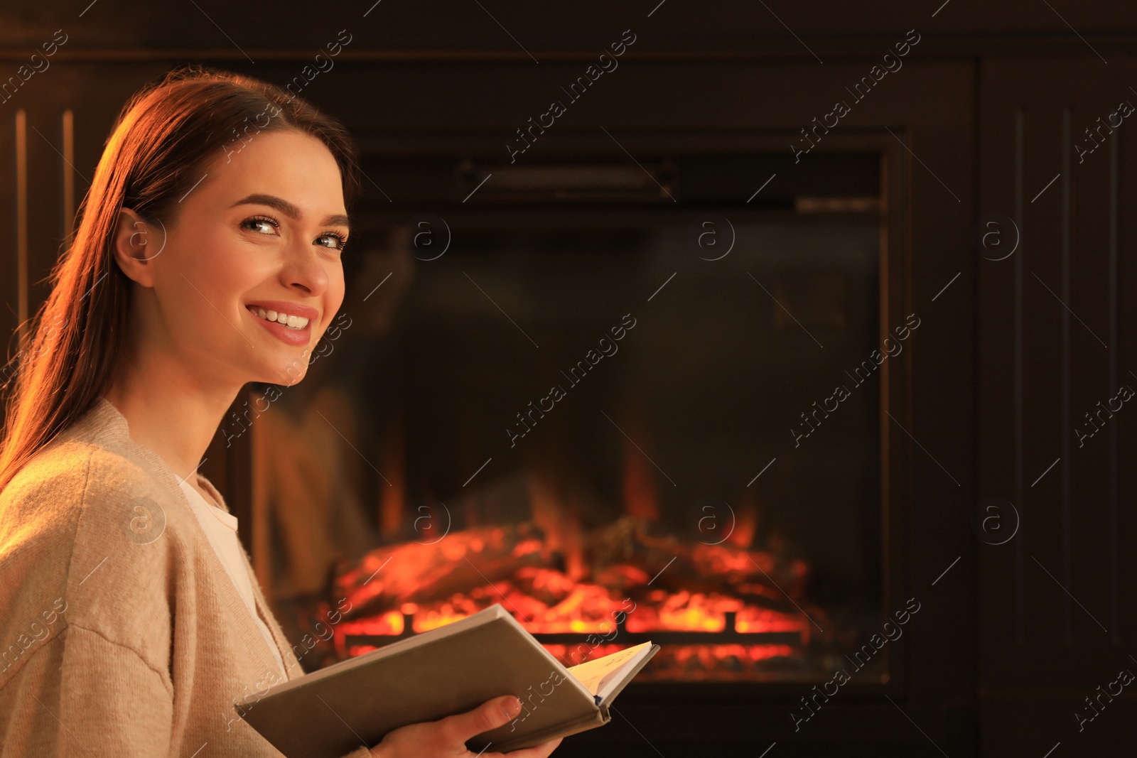 Photo of Young woman reading book near fireplace indoors. Cozy atmosphere