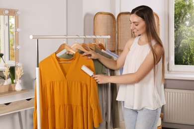 Photo of Young woman cleaning clothes with adhesive lint roller indoors