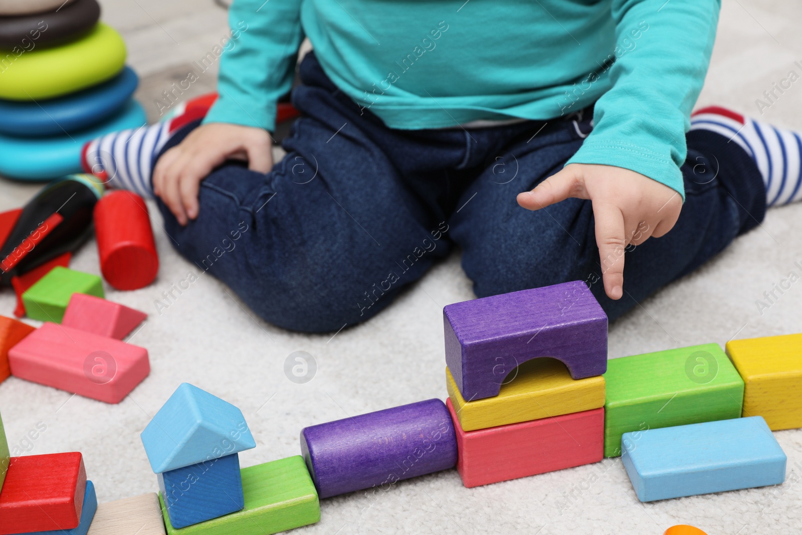 Photo of Little child playing with building blocks on carpet, closeup