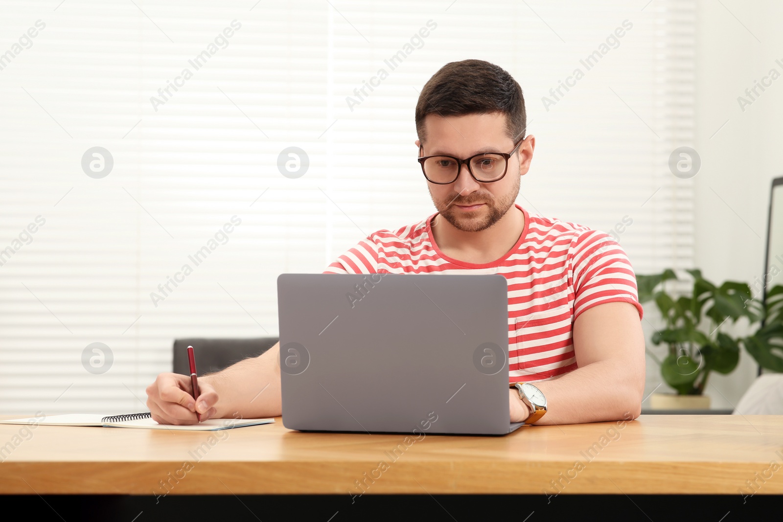 Photo of Man working with laptop at wooden table in room