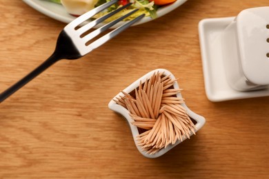 Photo of Holder with many toothpicks near food on wooden table, flat lay