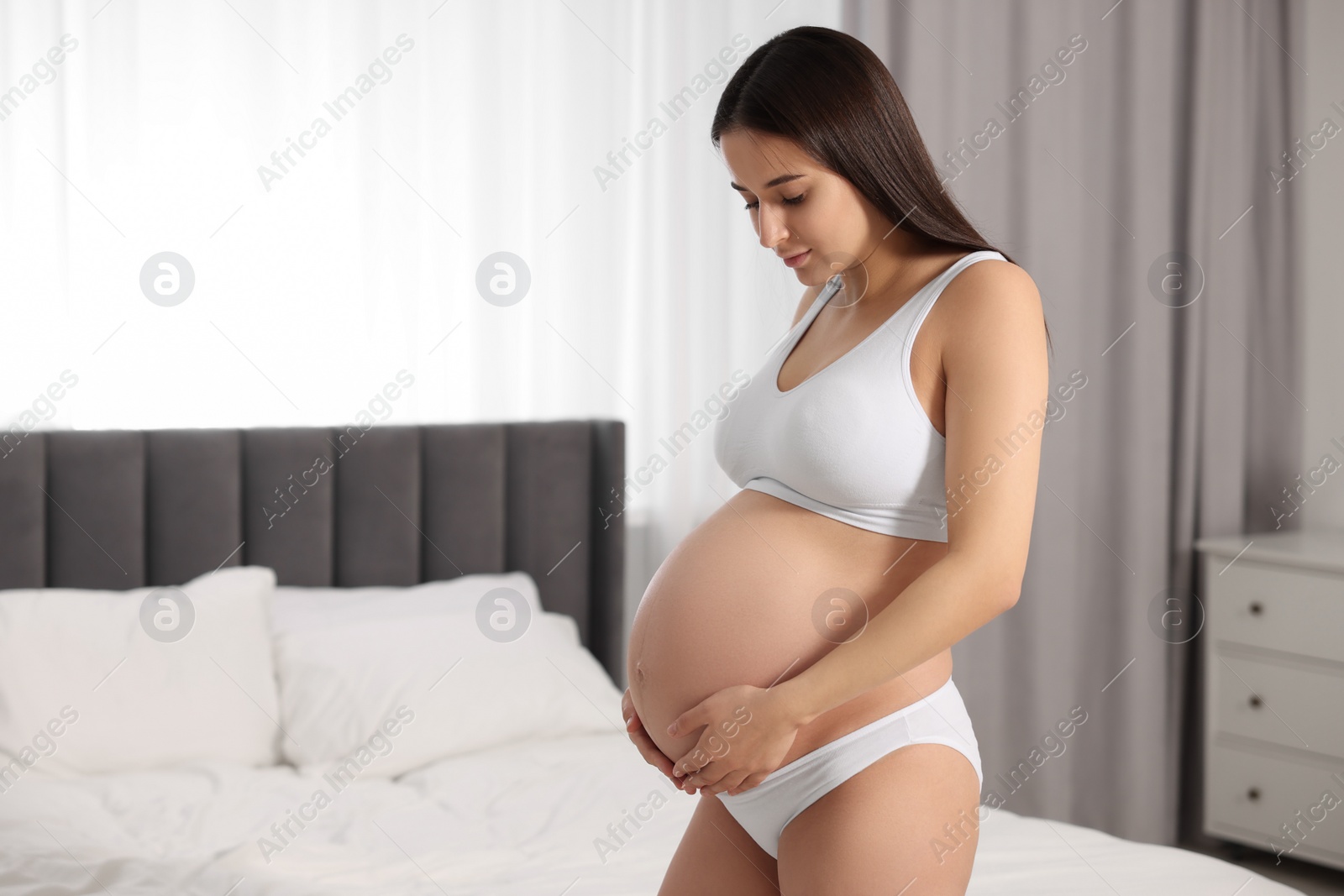 Photo of Beautiful pregnant woman wearing stylish comfortable underwear in bedroom, space for text