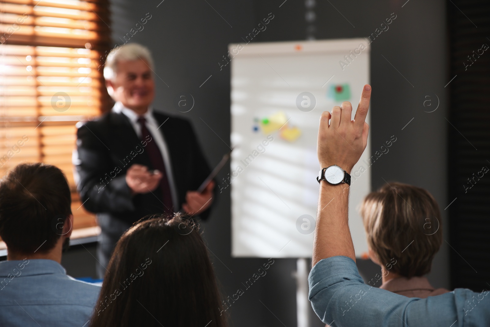 Photo of Man raising hand to ask question at seminar in office
