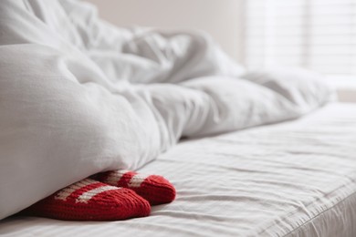 Woman wearing knitted socks under blanket in bedroom, closeup. Space for text