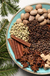 Different spices with nuts in bowl and fir branches on light gray table, flat lay