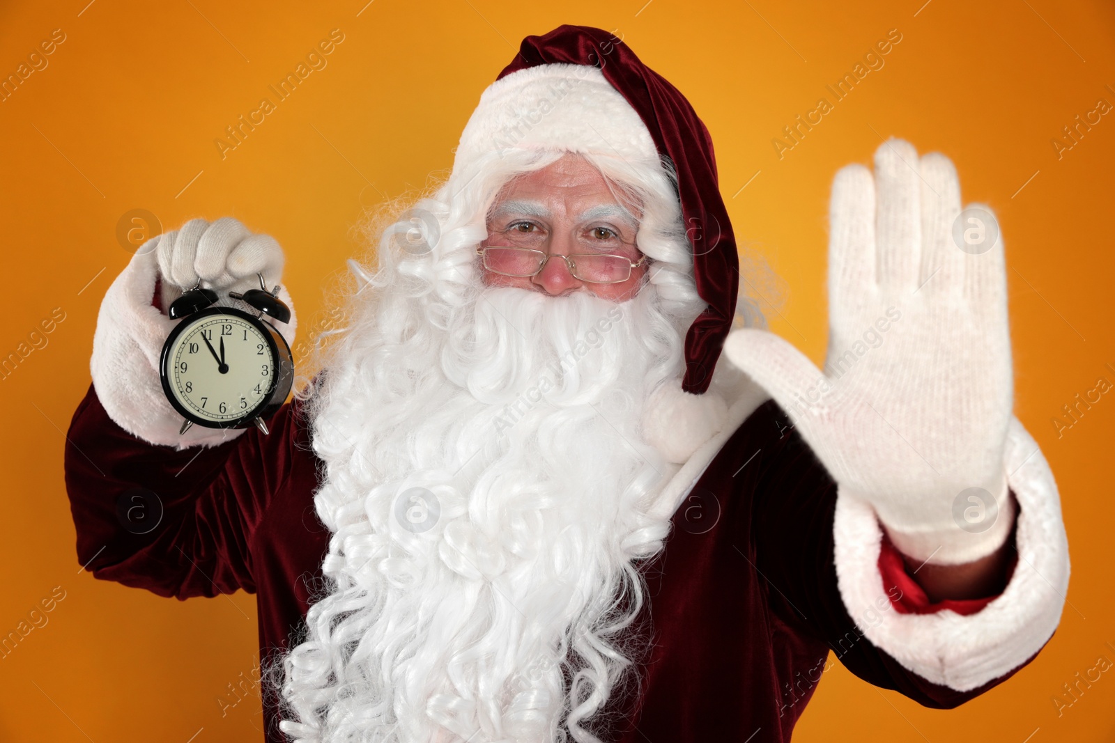 Photo of Santa Claus holding alarm clock on yellow background. Christmas countdown