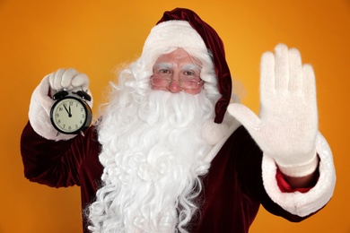 Photo of Santa Claus holding alarm clock on yellow background. Christmas countdown