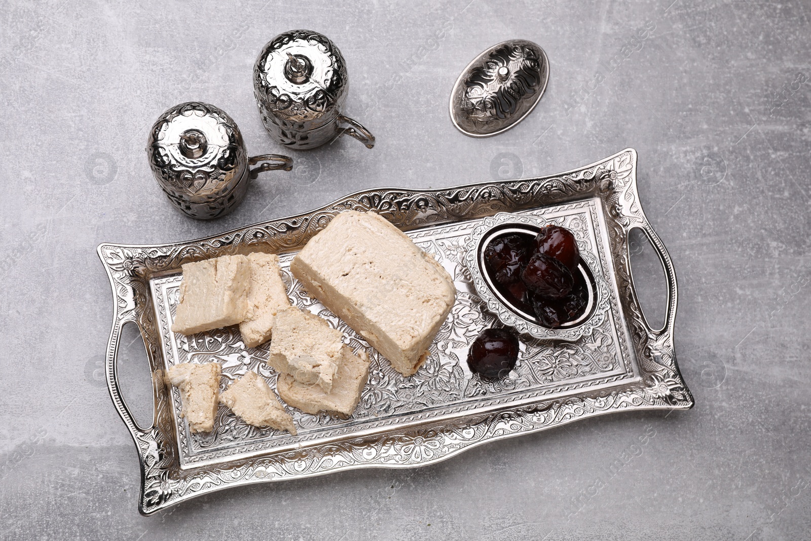 Photo of Pieces of tasty halva and dates served in vintage tea set on light grey table, above view