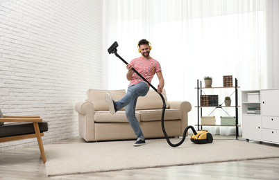 Photo of Young man having fun while vacuuming at home