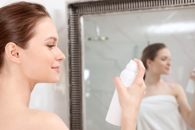 Young woman applying thermal water on face near mirror in bathroom. Cosmetic product