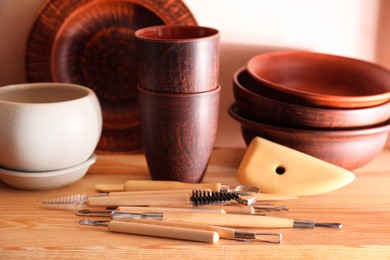 Set of different crafting tools and clay dishes on wooden table in workshop