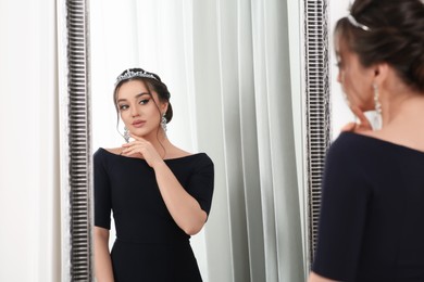 Photo of Beautiful young woman wearing luxurious tiara near mirror indoors