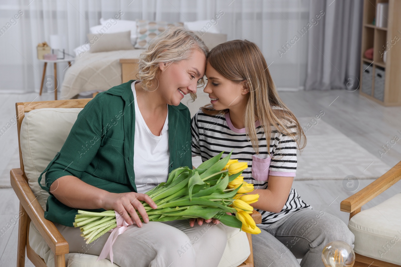 Photo of Young daughter congratulating her mom with flowers at home. Happy Mother's Day