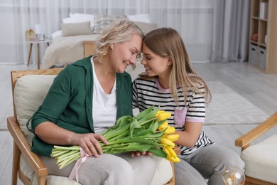 Photo of Young daughter congratulating her mom with flowers at home. Happy Mother's Day