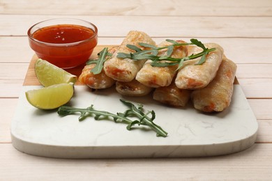 Photo of Tasty fried spring rolls, lime, arugula and sauce on light wooden table