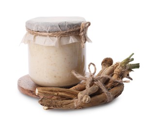 Glass jar of tasty prepared horseradish and roots isolated on white