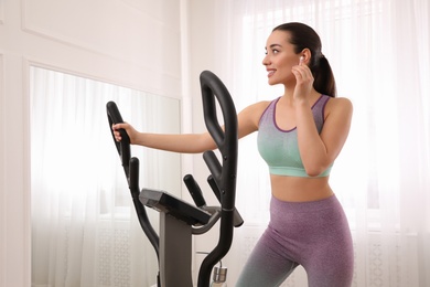 Woman using modern elliptical machine at home