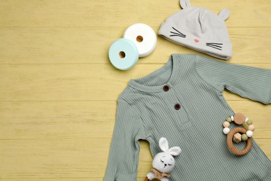 Flat lay composition with baby clothes and accessories on yellow wooden table. Space for text