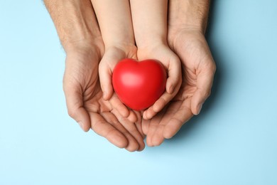 Photo of Man and kid holding red heart in hands on light blue background, top view
