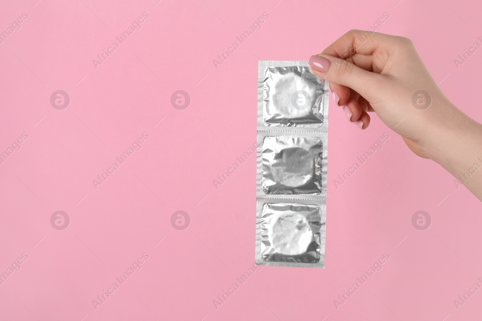 Photo of Woman holding condoms on pink background, closeup. Space for text