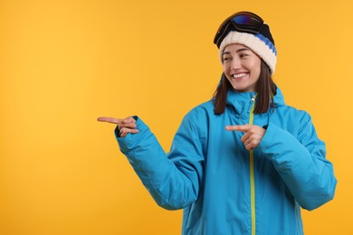 Photo of Winter sports. Happy woman with snowboard goggles pointing at something on orange background, space for text