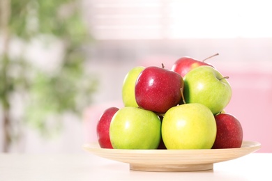 Photo of Plate with different sweet apples on table in room, space for text