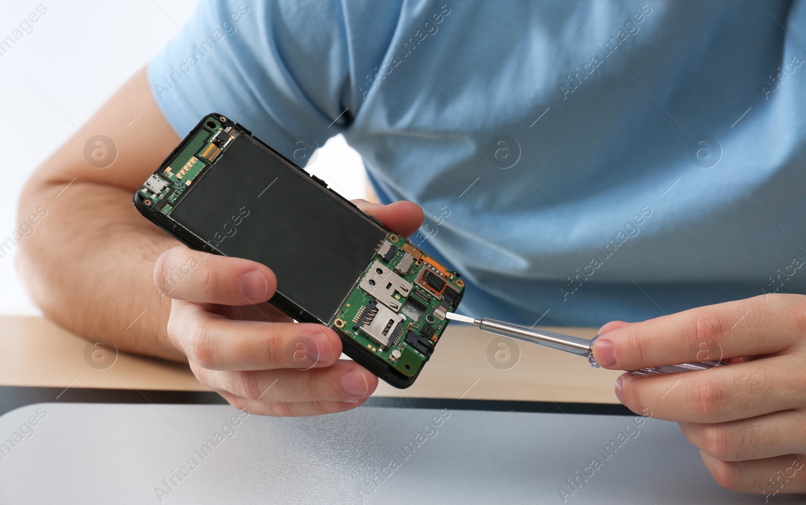 Photo of Technician repairing broken smartphone at table, closeup