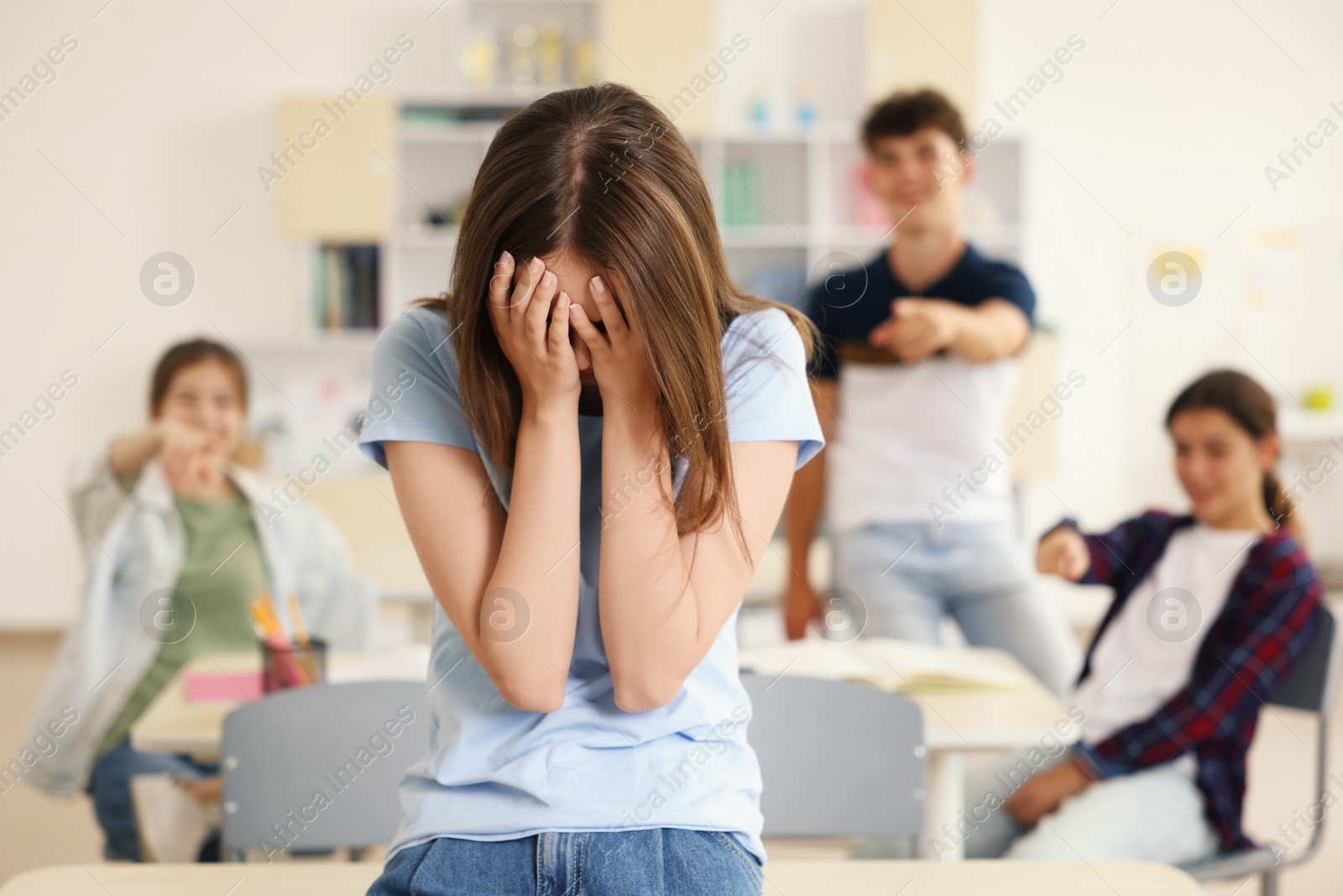 Photo of Teen problems. Students pointing at upset girl in classroom, selective focus