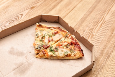 Photo of Cardboard box with pizza pieces on wooden table