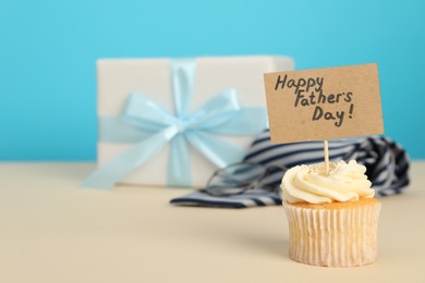 Photo of Happy Father's Day. Tasty cupcake with greetings and presents on beige table, closeup. Space for text