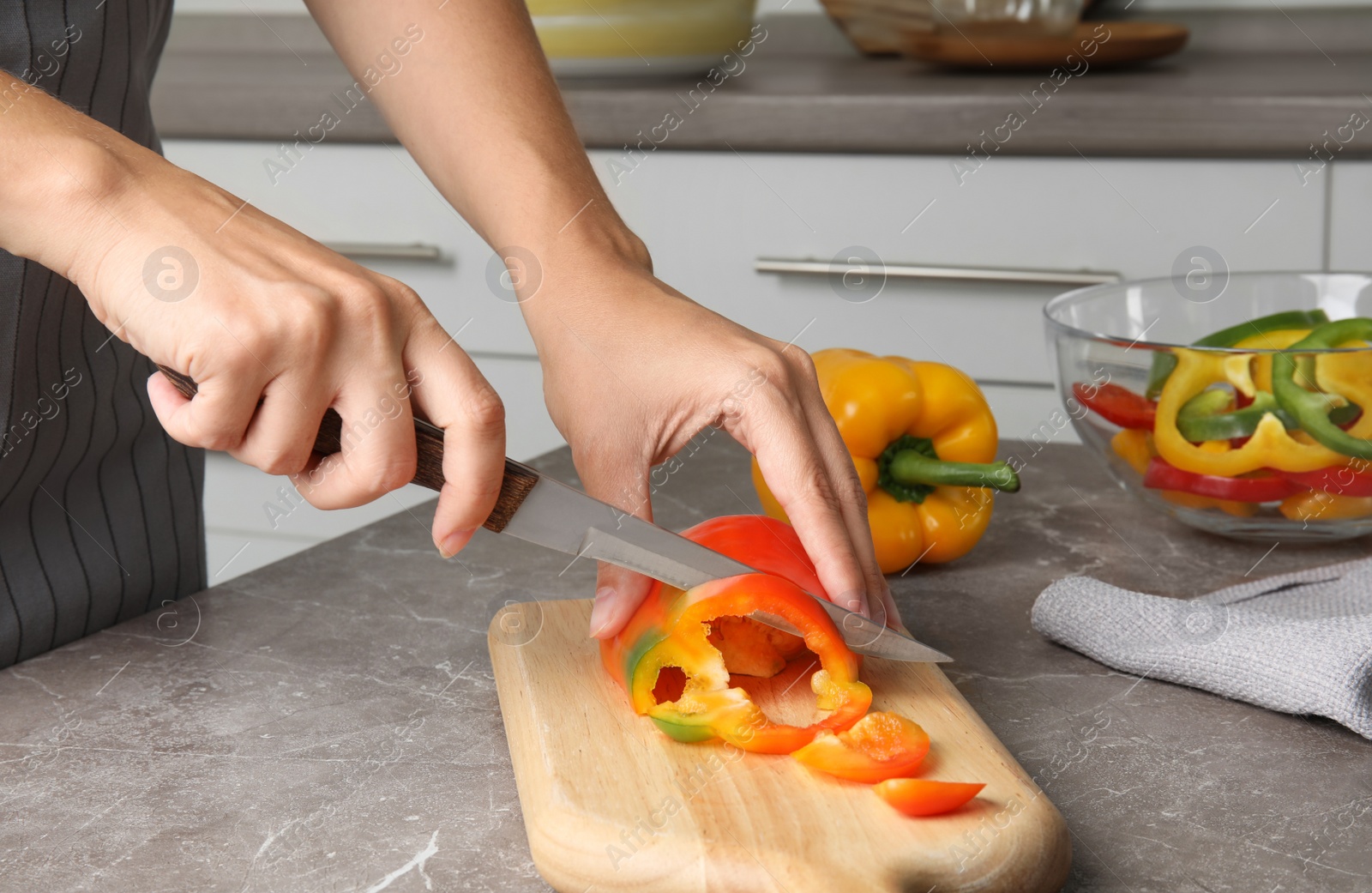 Photo of Woman cutting paprika pepper on wooden board at table, closeup