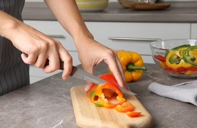 Woman cutting paprika pepper on wooden board at table, closeup