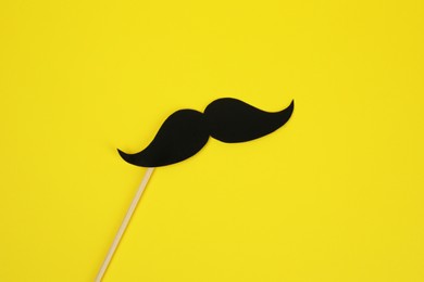 Photo of Fake paper mustache with stick on yellow background, top view