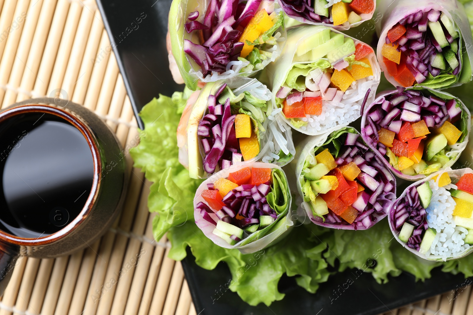 Photo of Delicious spring rolls and soy sauce on bamboo mat, top view