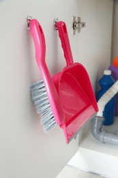 Brush and dustpan hanging on cabinet's door. Cleaning tools