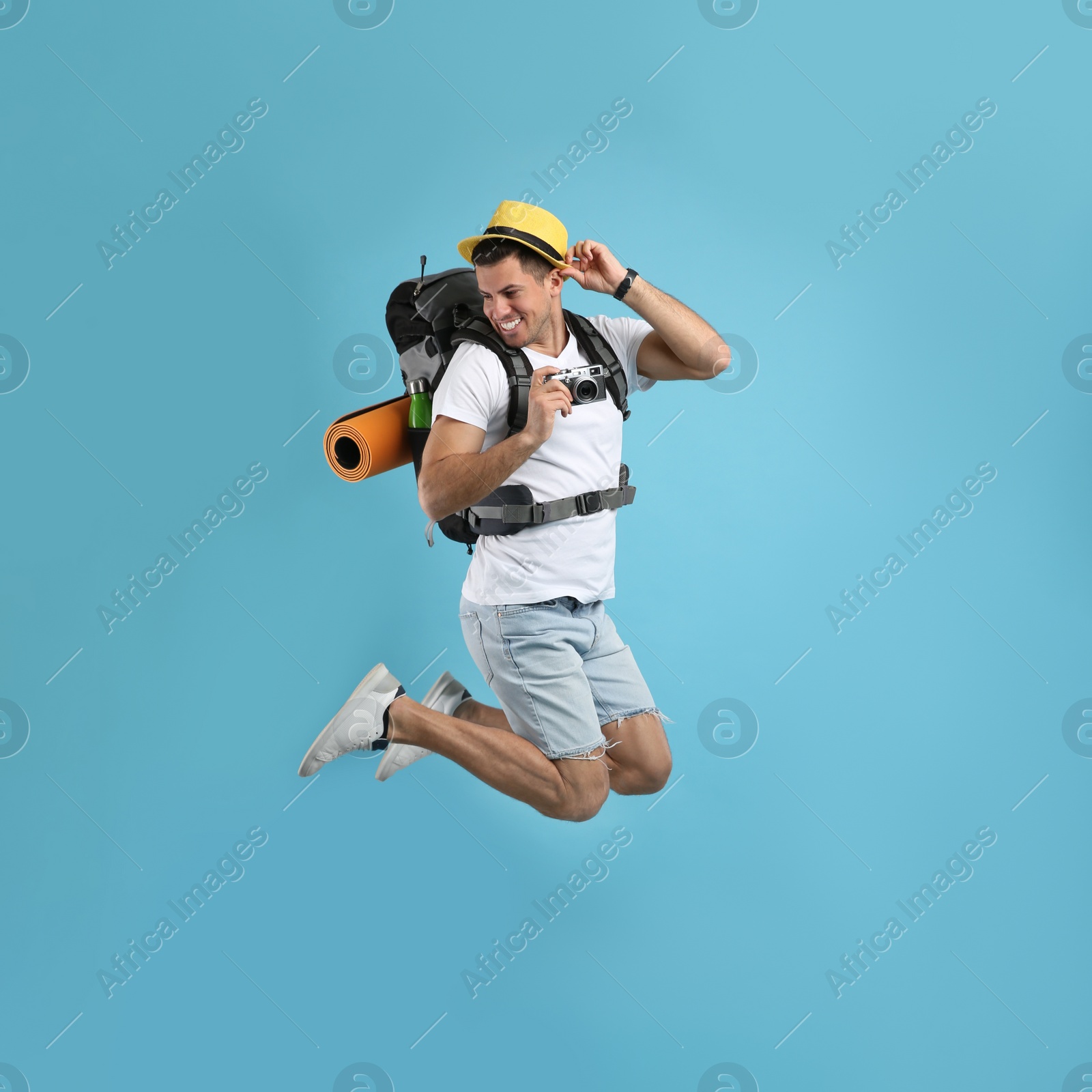 Photo of Male tourist with travel backpack and camera jumping on turquoise background