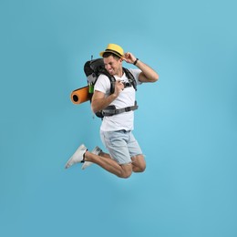 Photo of Male tourist with travel backpack and camera jumping on turquoise background