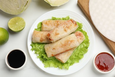 Photo of Delicious fried spring rolls served on white marble table, flat lay