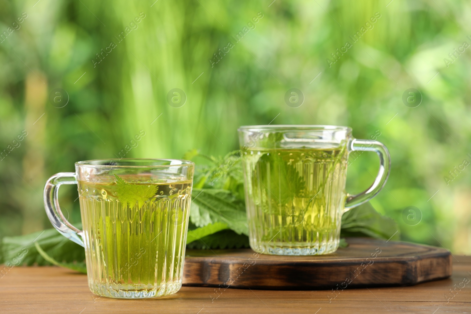 Photo of Aromatic nettle tea and green leaves on wooden table outdoors